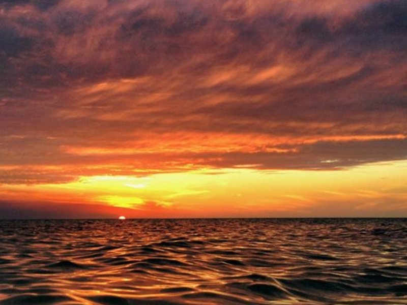 Un atardecer en Holbox con siluetas de turistas y locales sobre el muelle empapados en la brillante luz naranja