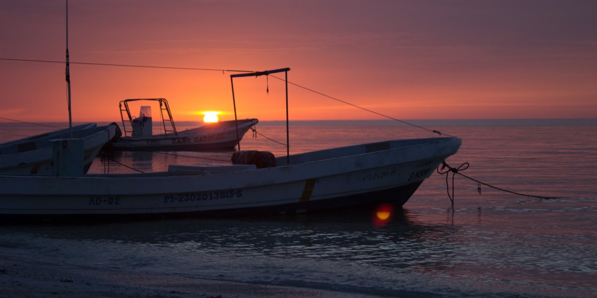 Two small fishing boats anchored on the beach of Holbox with a purple sunset