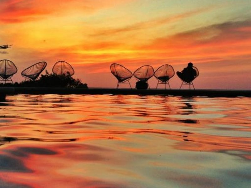 Un atardecer en Holbox con siluetas de turistas y locales sobre el muelle empapados en la brillante luz naranja