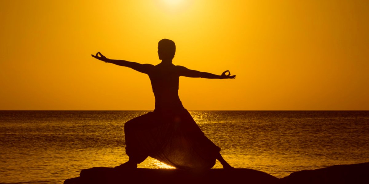 La silueta de una yogi posando al lado del mar con el cielo y sol amarillos atrás 