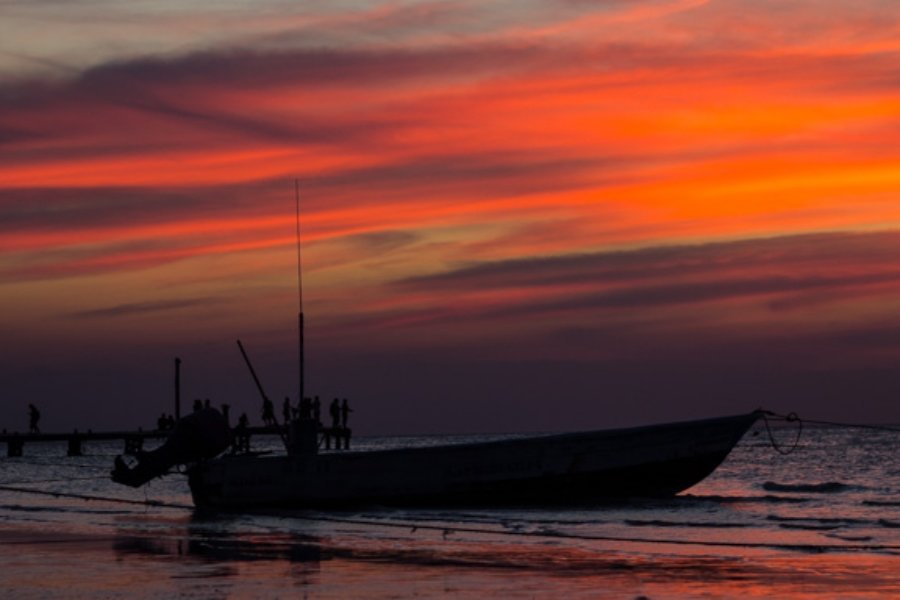 Un atardecer en Holbox con siluetas de turistas y locales sobre el muelle empapados en la brillante luz naranja