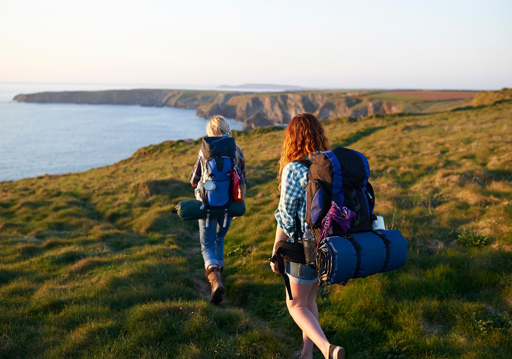 Två vandrare med ryggsäckar med havet i bakgrunden