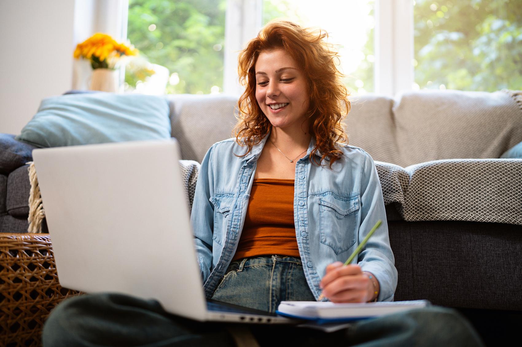 Kvinna sitter framför soffa med laptop och skrivblock