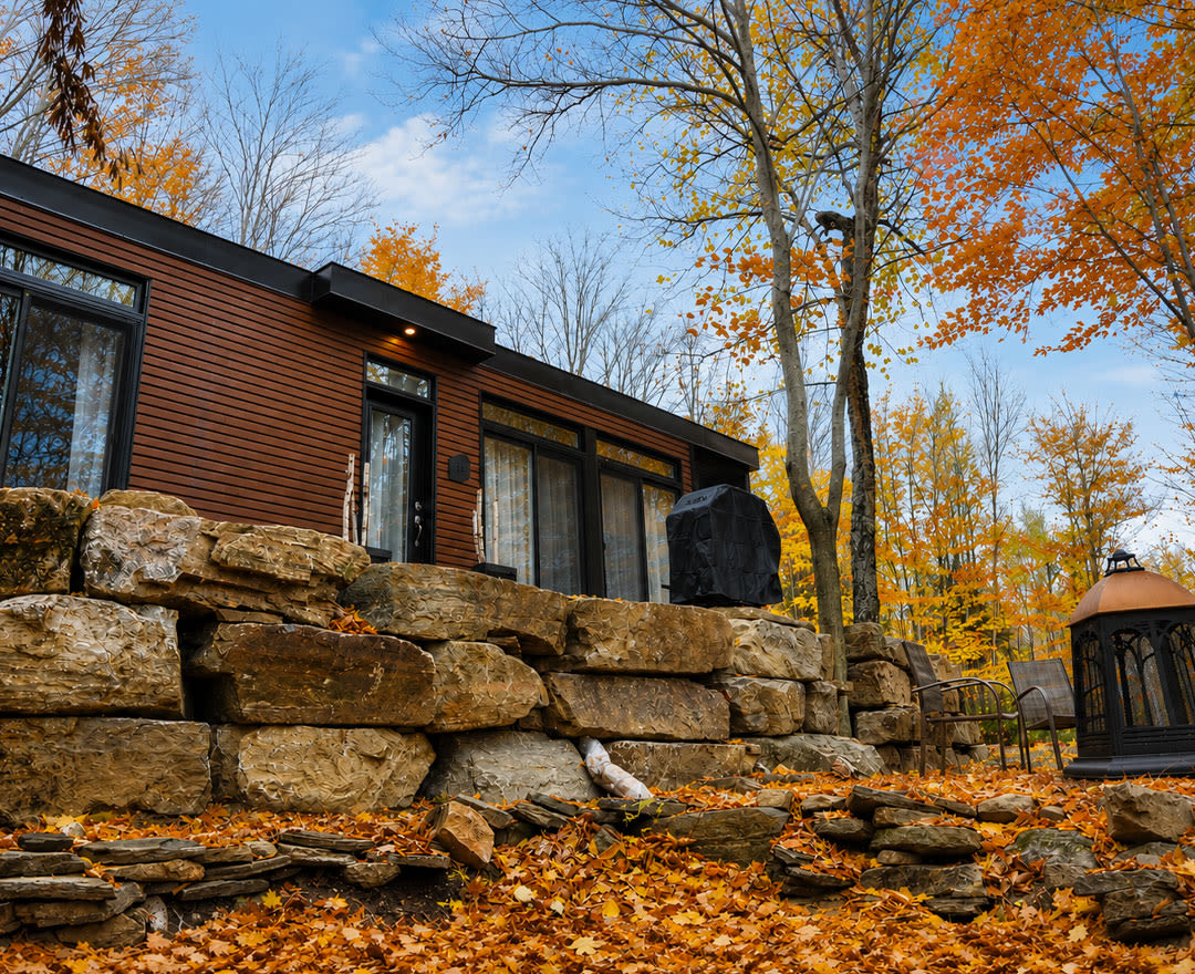 Natur'Eau Spa & Chalets: Un chalet moderne niché en pleine forêt, sublimé par les couleurs chaleureuses de l’automne et un ciel bleu lumineux.