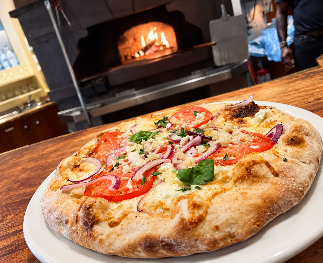 Deux pizzas généreusement garnies accompagnées de verres de vin rouge pour une expérience gourmande et conviviale.