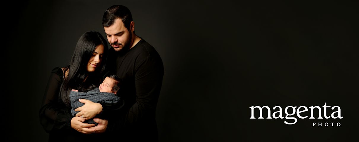 Magenta Photo: Un couple pose tendrement avec leur nouveau-né emmailloté dans leurs bras, dans une ambiance intime et chaleureuse.