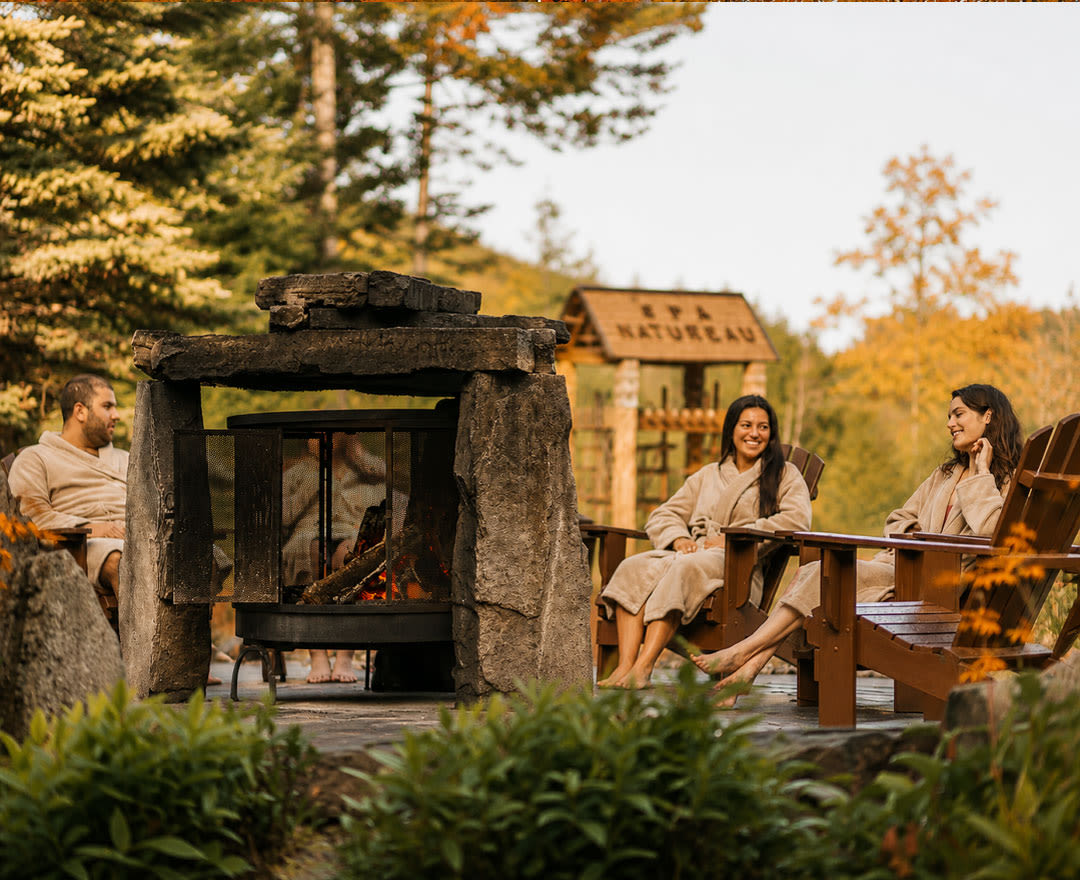 Natur'eau Spa & Chalets: Des gens profitent d’un moment de détente autour d’un feu extérieur, dans un décor naturel aux douces couleurs automnales