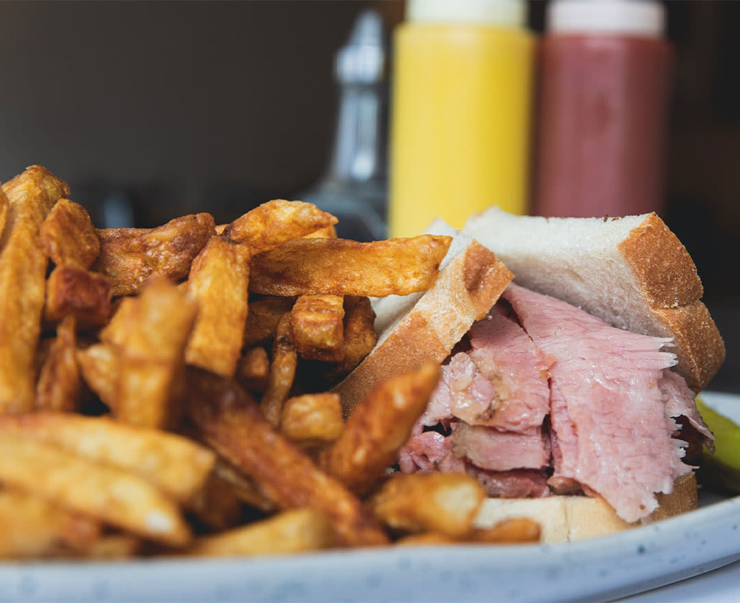 Sandwich au smoked meat garni de fines tranches de viande fumée ET sandwich au smoked meat accompagné de frites, de salade de chou, de cornichons et d'une bière