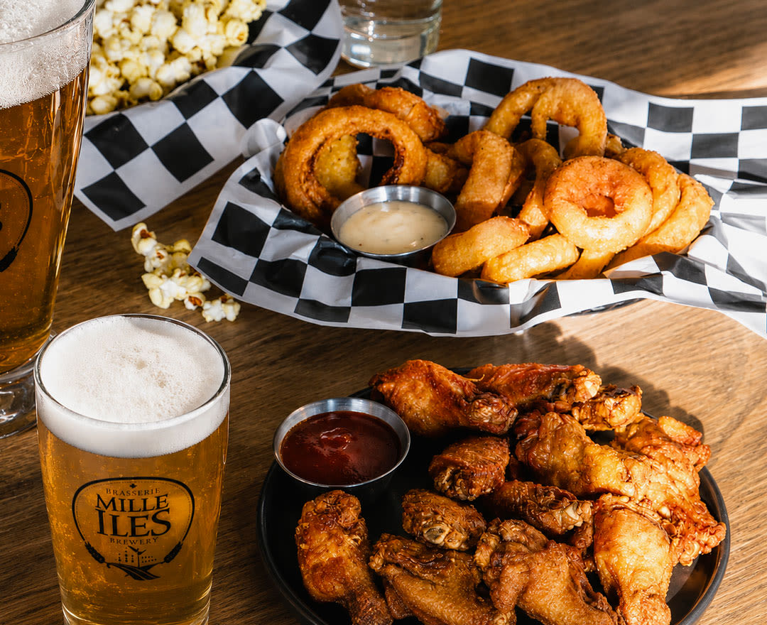 Des bières artisanales accompagnées d’ailes de poulet croustillantes, de rondelles d’oignon et de popcorn