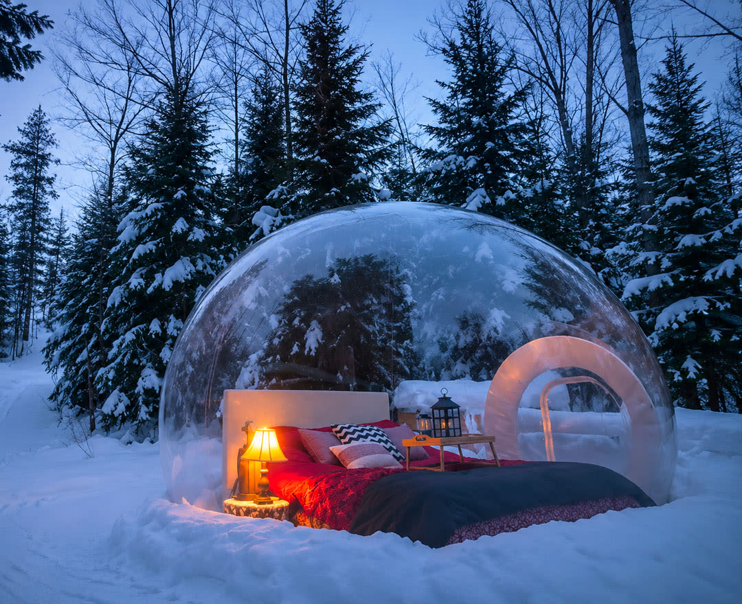 Cavaland - Lit en dôme transparent dans une forêt enneigée, éclairé par une lampe et une lanterne, ambiance chaleureuse et hivernale.