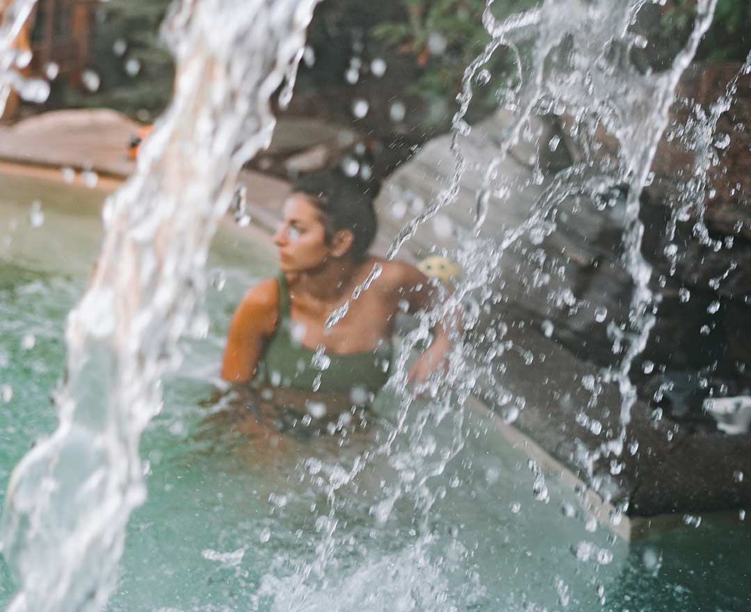 Natur'Eau Spa & Chalets: Une femme profite d’un moment de détente dans un bassin extérieur sous une chute d’eau rafraîchissante.