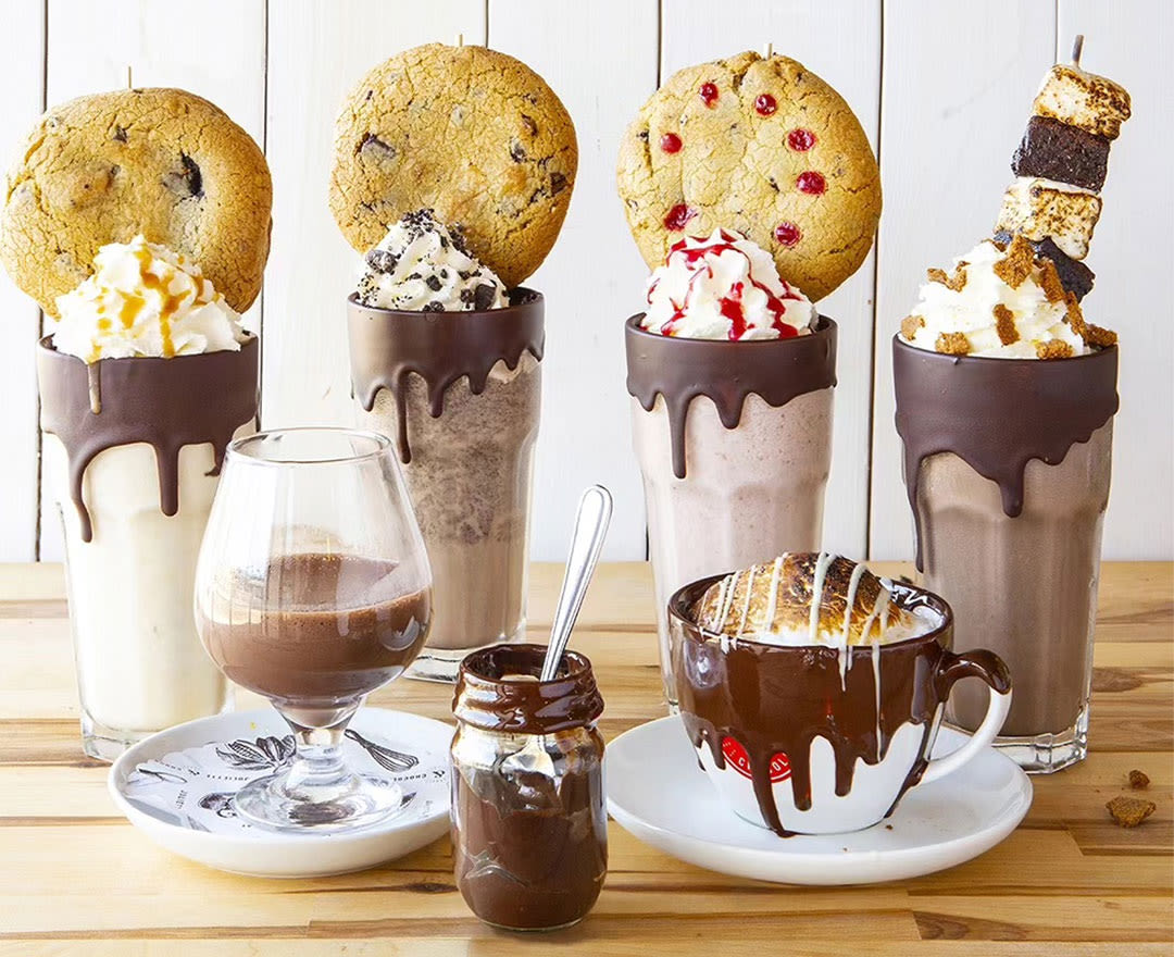 Un brownie garni de noix de pécan accompagné d’un assortiment décadent de boissons chocolatées et de milkshakes gourmands.