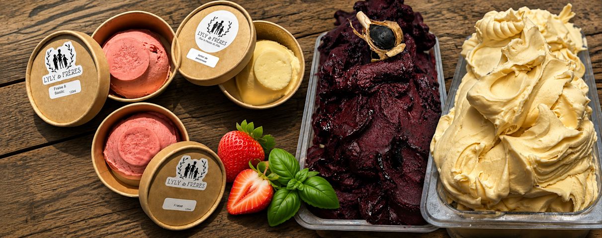 Un assortiment coloré de glaces artisanales aux fruits est présenté avec des fraises fraîches et du basilic.