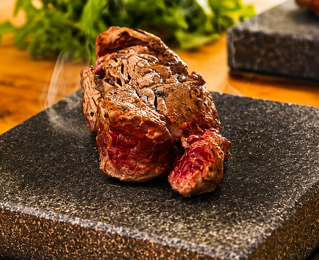 Un steak saignant sur une pierre chaude, entouré de laitue verte et rouge, sur une table en bois.