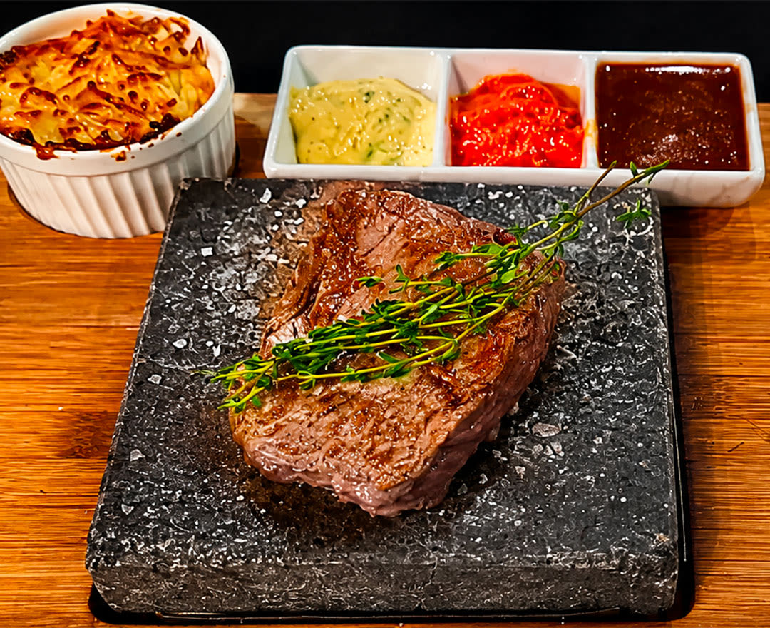 Assiette de viande grillée avec germes, légumes colorés et sauces variées sur une table en bois.