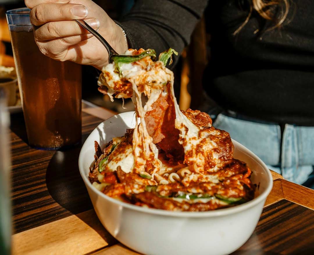 Un homme qui mange un sandwich au poulet frit et frites, des pizzas sur la table
