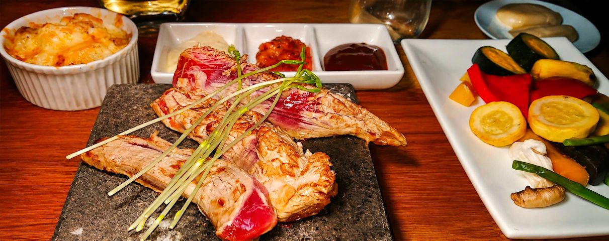 Tranches de viande grillée avec germes, légumes colorés et gratin de pommes de terre sur une table en bois.