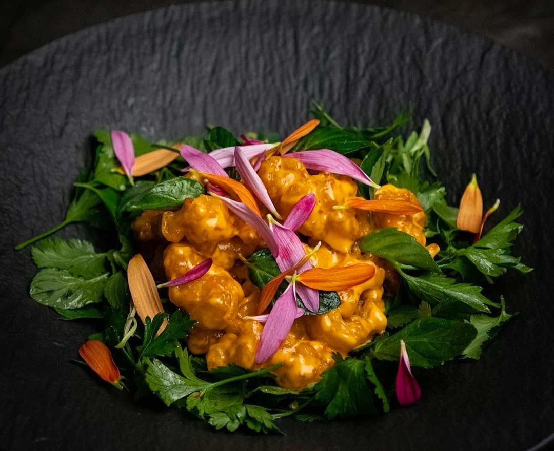 Steak grillé avec queue de homard, légumes colorés et herbes dans une poêle noire sur une assiette blanche.