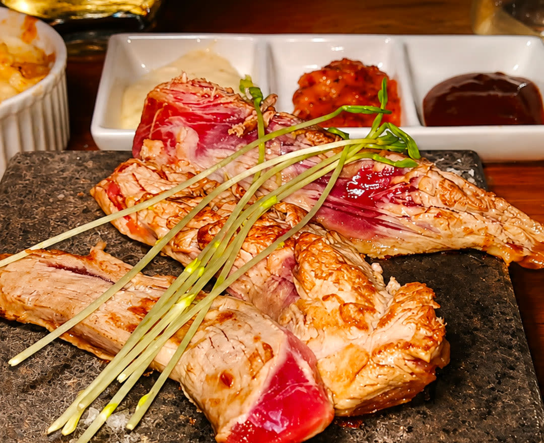 Steak sur pierre chaude avec herbes, gratin, sauces variées, légumes frais et champignons sur planche en bois.