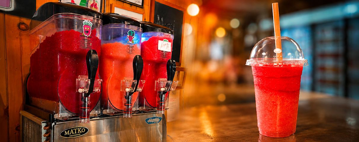Des boissons glacées rouges sont servies à partir de machines à granité, avec un verre prêt à être dégusté.