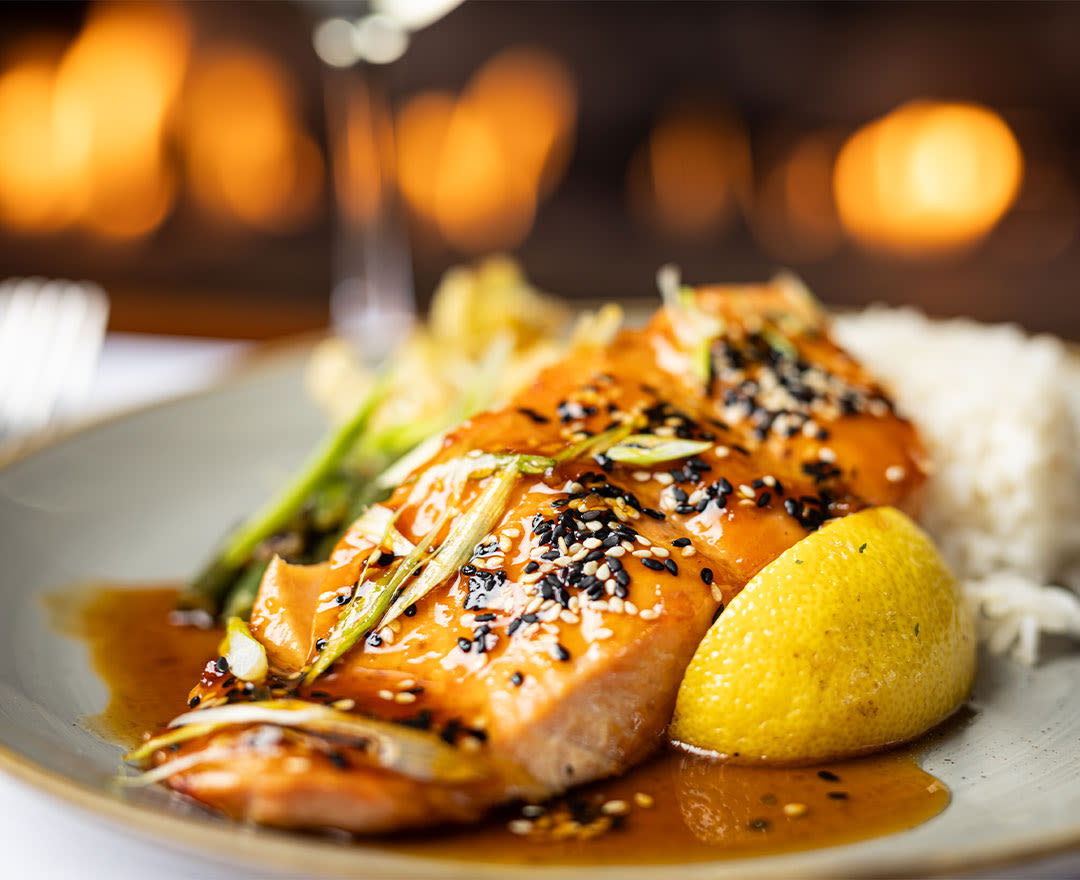 Un pavé de saumon glacé à l’orientale, garni de graines de sésame et accompagné de riz, de légumes et de citron.
