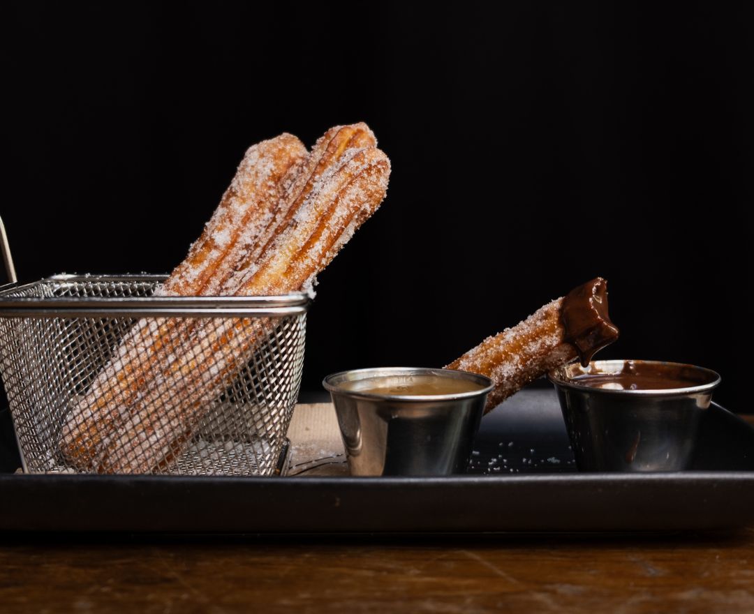 Trois assiettes de churros dorés accompagnés de sauces au chocolat et au caramel.