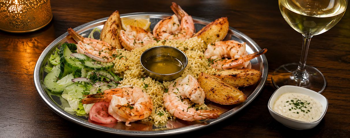 Une généreuse assiette de crevettes grillées, servie avec du riz aux herbes, une salade fraîche, des quartiers de pommes de terre, une sauce tartare et un verre de vin blanc.