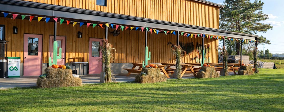 Une grange rustique en bois décorée de fanions colorés, de bottes de foin et de cactus crée une ambiance champêtre et accueillante.
