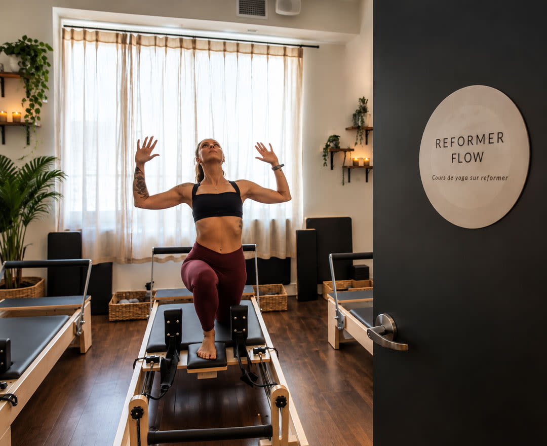 Idolem: Une femme pratique un exercice de Pilates sur Reformer dans un studio chaleureux et épuré.