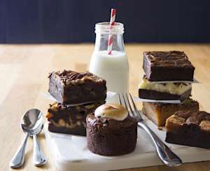Juliette&Chocolat: Un assortiment de brownies aux garnitures variées, accompagné d’une bouteille de lait et présenté sur une planche blanche.