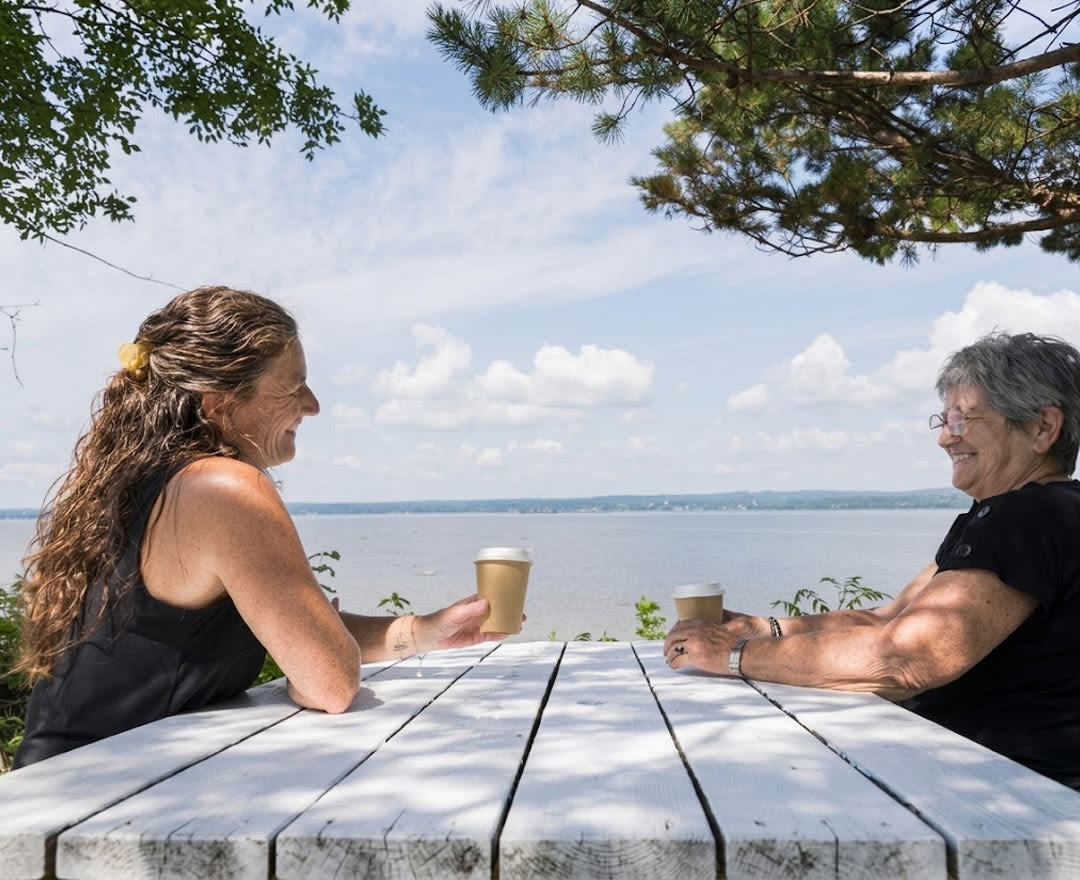 Deux personnes partagent un moment de détente autour d’un café avec une magnifique vue sur le fleuve.