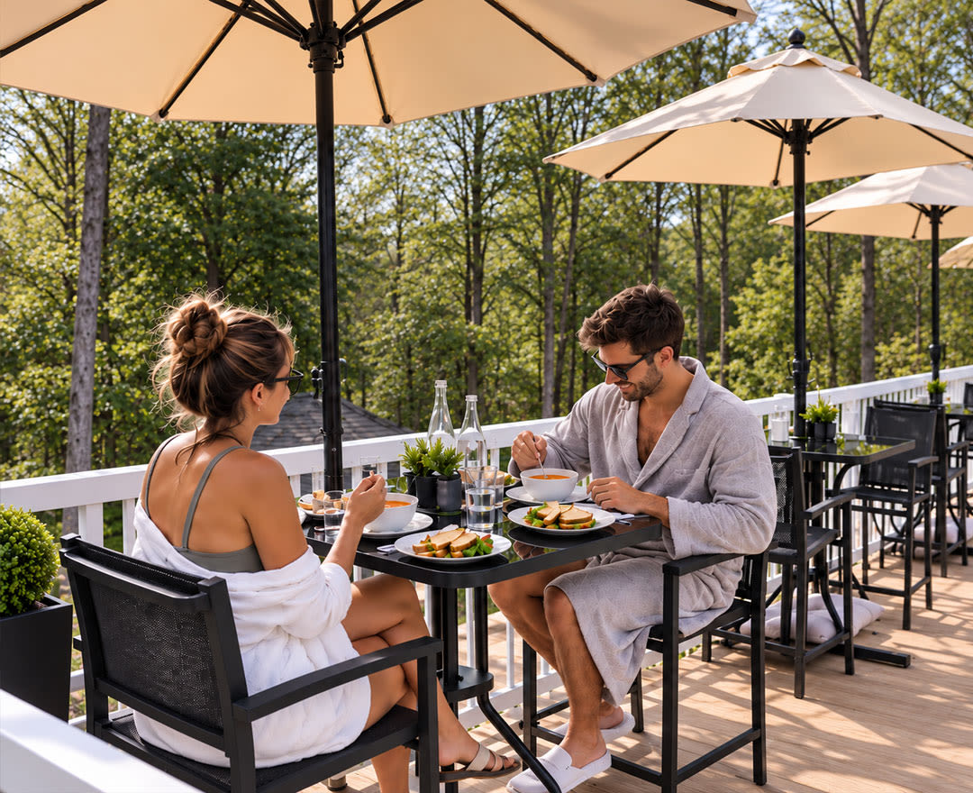 Un couple savoure un repas sur une terrasse ensoleillée, entourée de verdure.