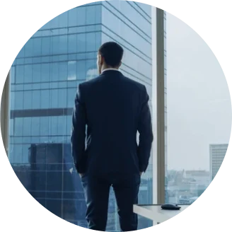 Man wearing a suit standing in front of a window looking at a skyscraper
