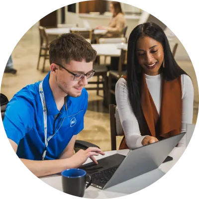 Two P&G employees sitting at a desk smiling and looking at a laptop in one of P&G's meeting spaces.