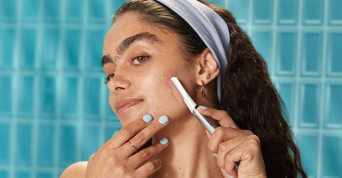 A young woman wearing a headband uses a razor to remove facial hair.