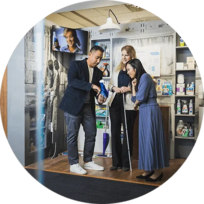 A man holds and points at a bottle of dish soap. Two women stand next to him and lean in to take a closer look.