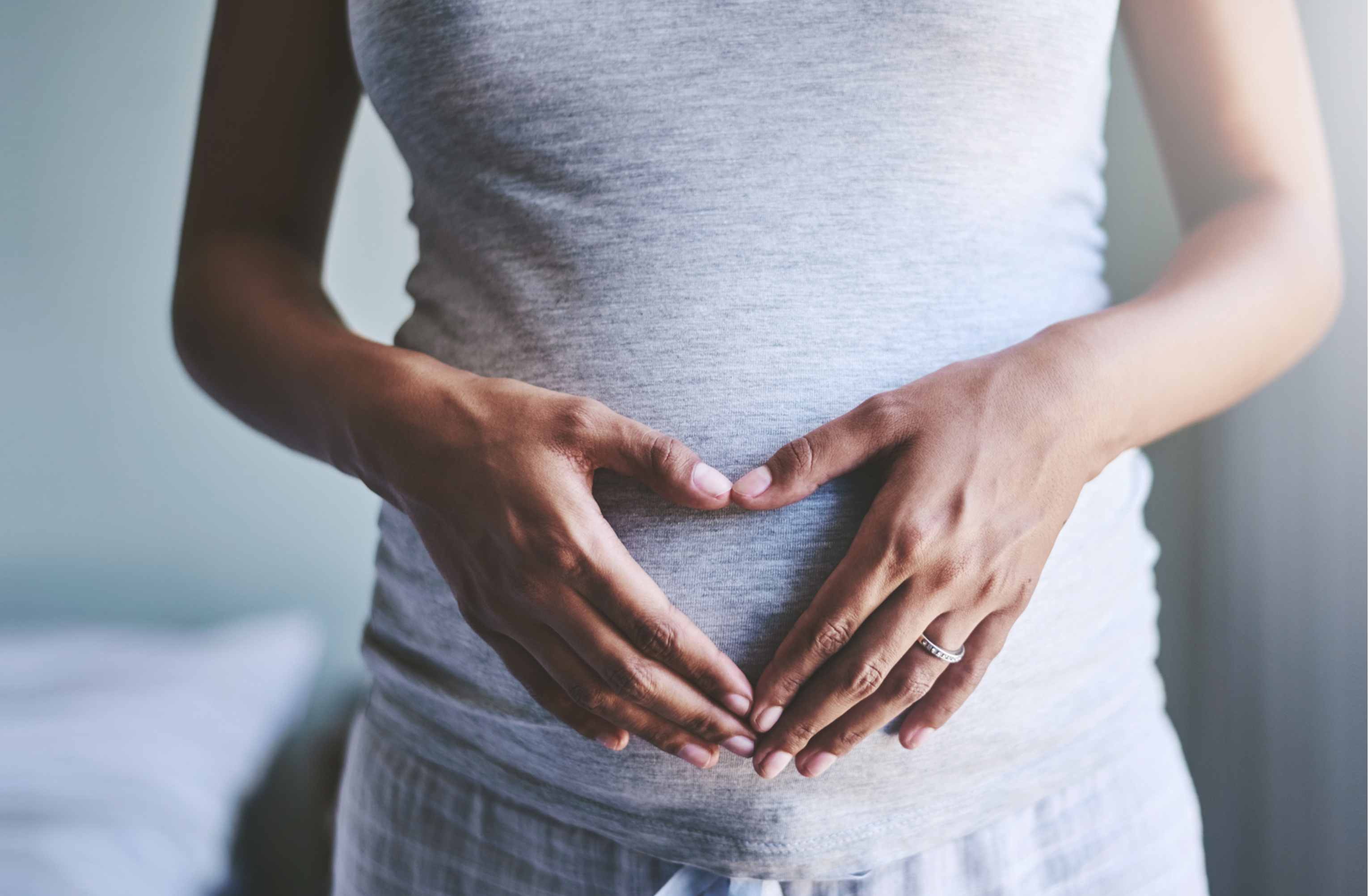 Female in gray shirt with hands resting on pregnant stomach