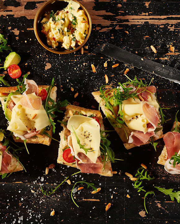 Käse-Baguette mit Basilikum-Pinienkern-Butter, Parmaschinken, Avocado, Rucola und Kirschtomaten