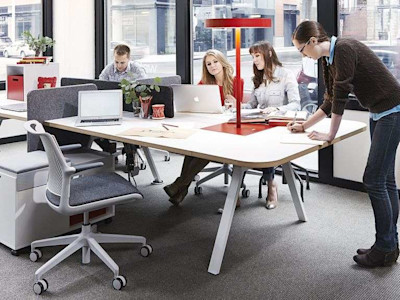 People at work around collaborative desk in front of big windows with light