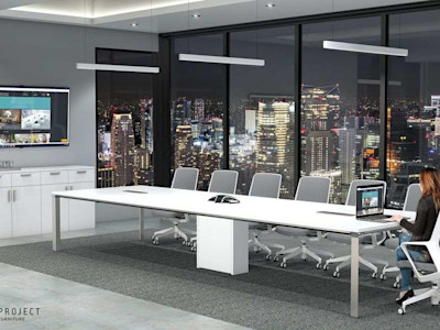 Woman sitting at a long white executive conference table looking at a monitor.