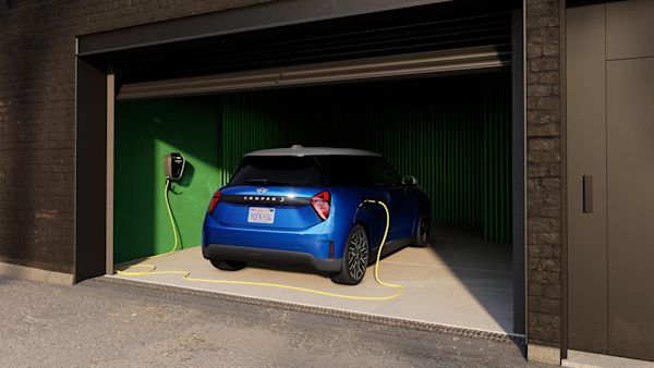 Blue MINI Cooper Electric charging inside a green-walled garage, connected to a yellow cable from a wall-mounted charging station.