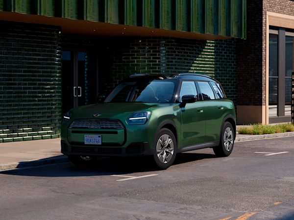 Green MINI Countryman electric parked on a city street in front of a modern building with green tiles and large windows.