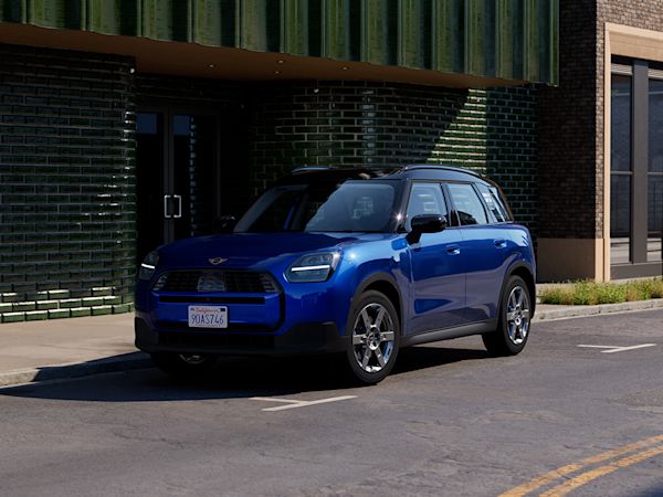 A blue MINI Countryman parked on the side of a street in front of a modern building with green and brick walls.
