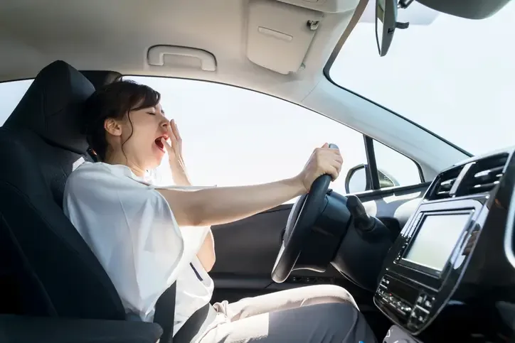 Conductora bostezando al volante mostrando signos de fatiga y somnolencia durante la conducción
