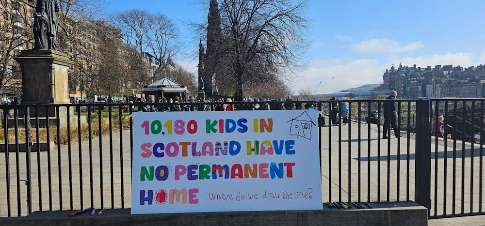 A banner attached to a railing in Princes Street Gardens in Edinburgh. The banner says that 10,180 kids in Scotland have no permanent home.