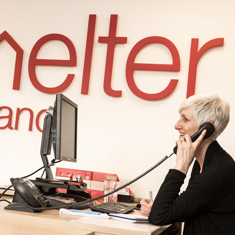 A Shelter adviser at her desk, on the phone, smiling