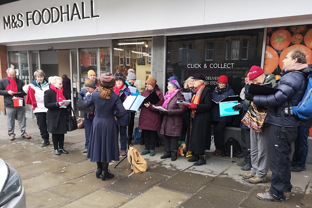 A choir singing outside of Marks and Spencer Food Hall in Edinburgh
