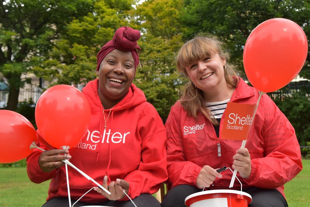 Two woman with Shelter Scotland hoodies on holding balloons and a fundraising bucket