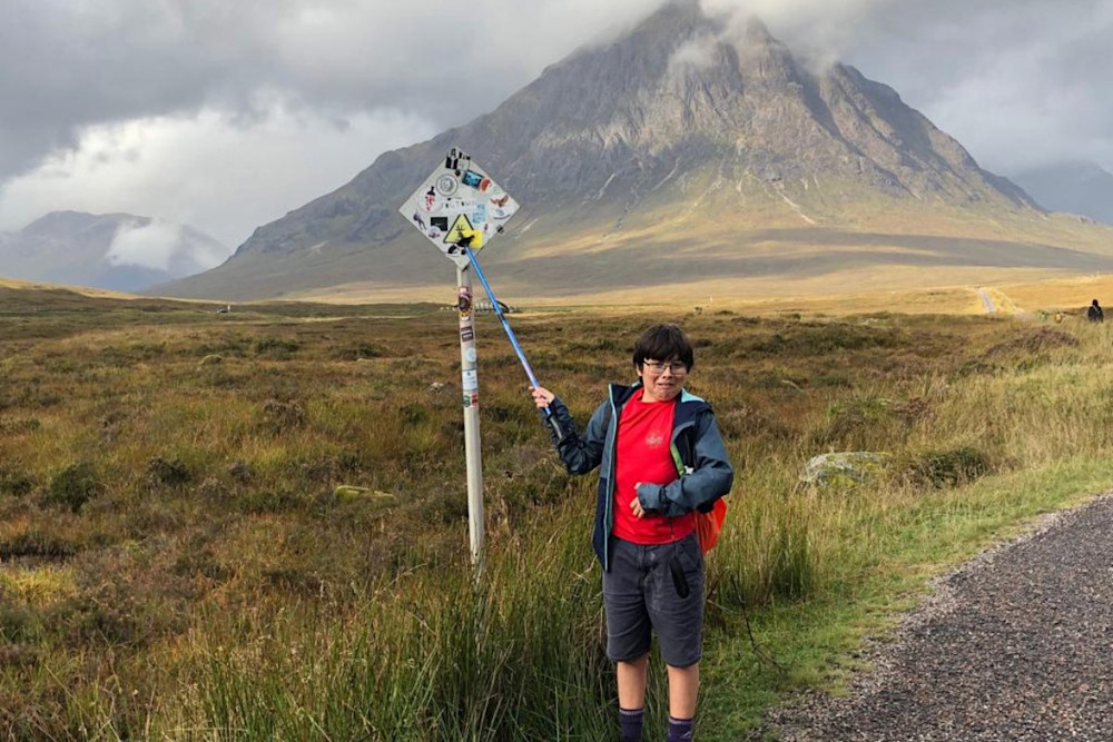 Keir standing in front of a sign with a Munro shrouded in cloud behind him.
