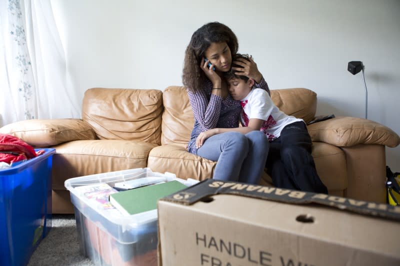 A woman on the sofa, holding her child, looking stressed and talking on the telephone